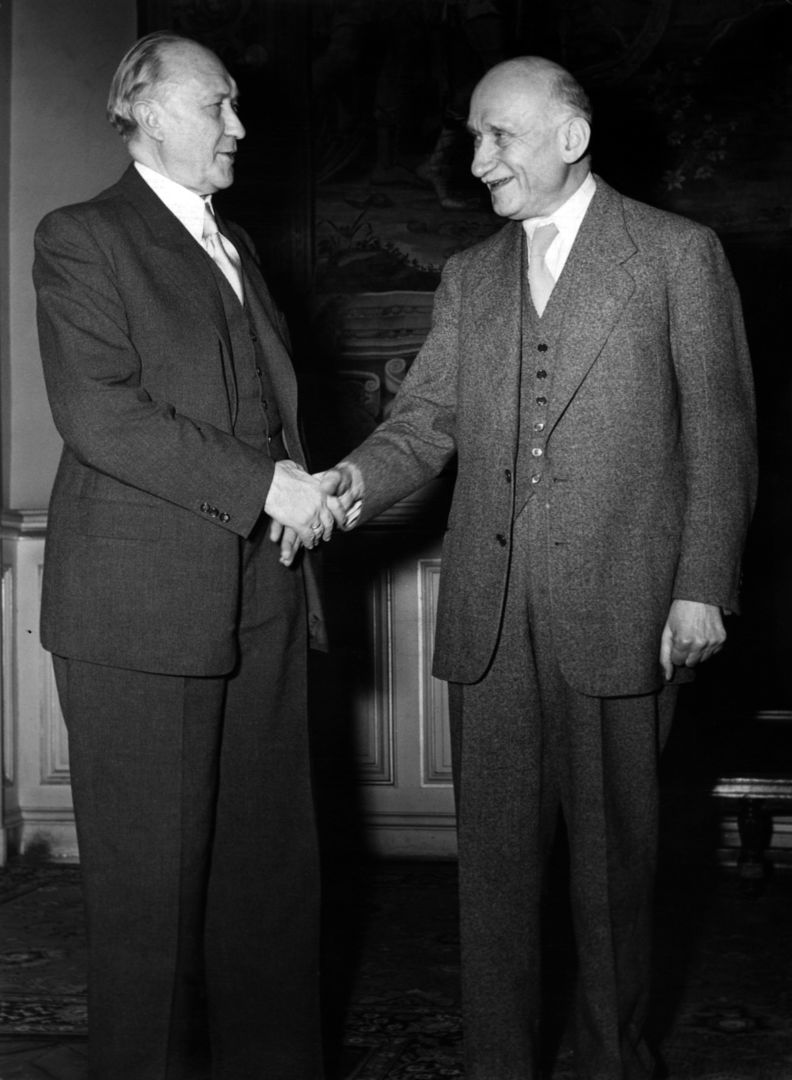Bundeskanzler Konrad Adenauer schüttelt Robert Schuman die Hand.