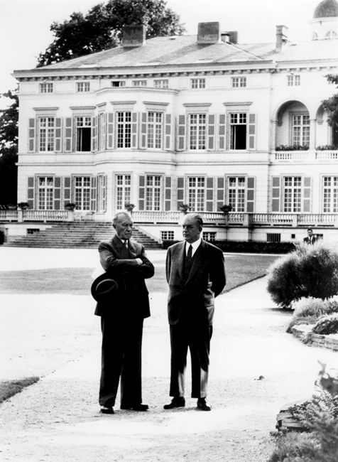 Zwei Männer nebeneinander in einem großen Garten , hinter ihnen ein Palast 