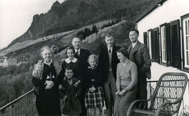 Schwarz-Weiss-Aufnahme von Familie Adenauer vor einem Haus und bergiger Landschaft