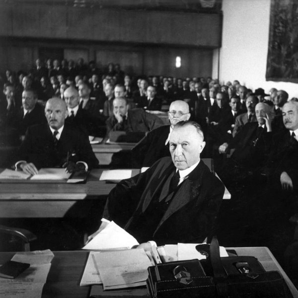Konrad Adenauer sitzend in einem großen Saal mit vielen anderen Personen