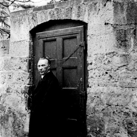 Konrad Adenauer steht vor einer alten Tür in einer alten Mauer