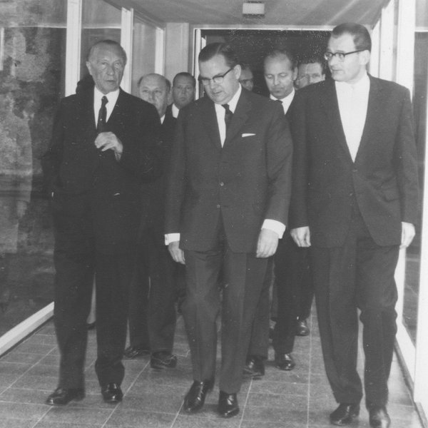 Konrad Adenauer geht mit mehreren Männern einen Gang entlang.