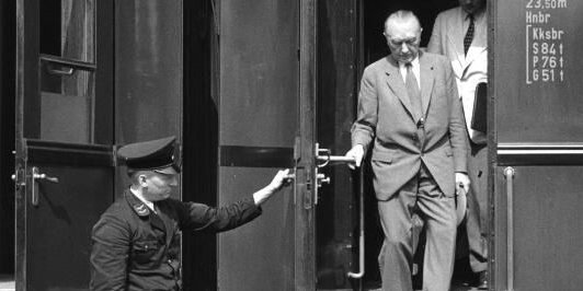 Adenauer steigt aus einem Zug aus. Ein Schaffner hält ihm die Tür auf.