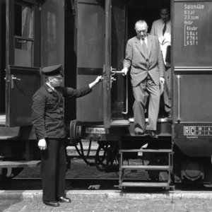 Adenauer steigt aus einem Zug aus. Ein Schaffner hält ihm die Tür auf.