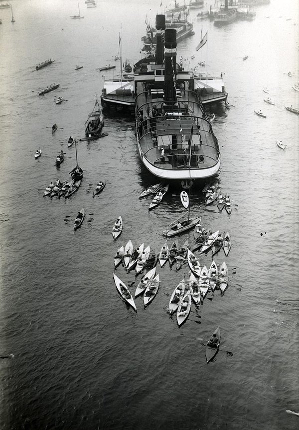 Schwarz-Weiss-Aufnahme von einem Schiff und zahlreichen Kanus