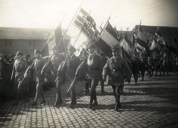 Schwarz-Weiss-Aufnahme von marschierenden Soldaten mit Flaggen