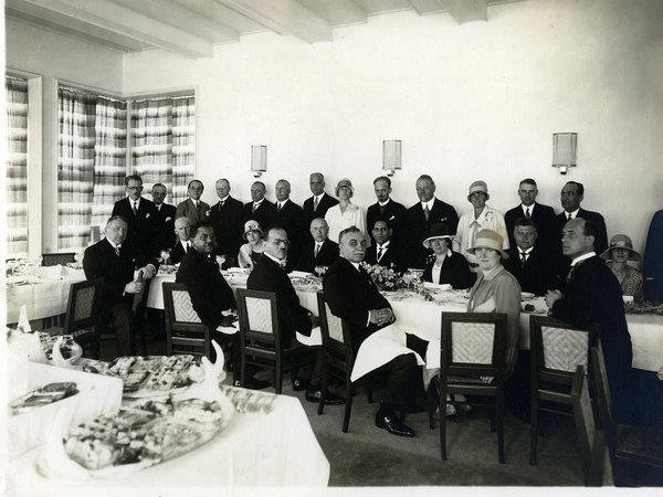 Schwarz-Weiss-Aufnahme von einer Gruppe Menschen an einem langen Esstisch 