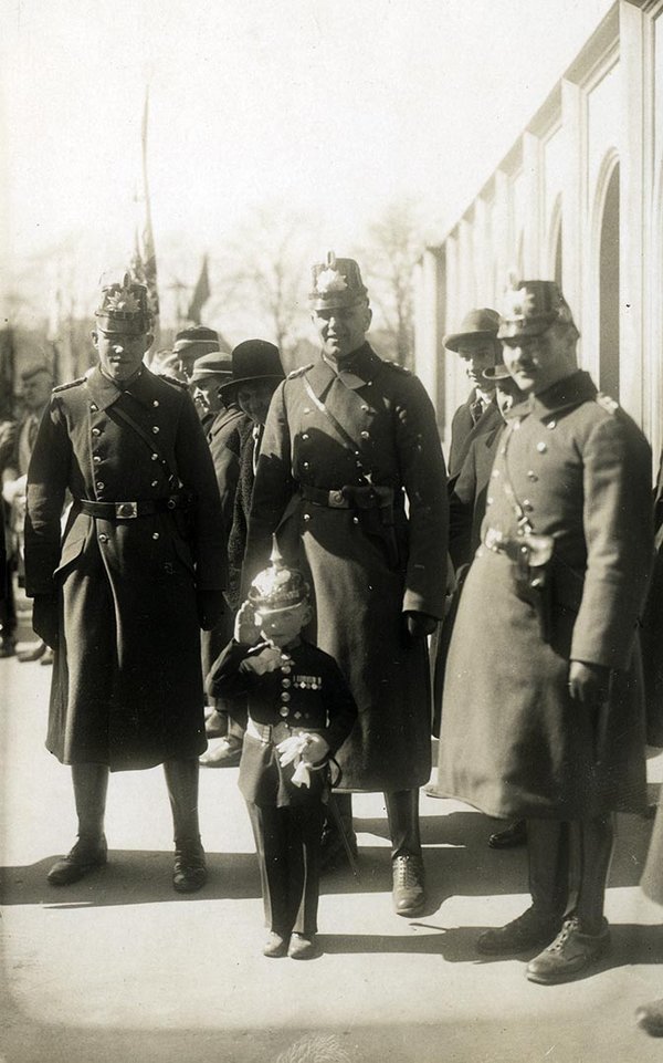 Schwarz-Weiss-Aufnahme von drei Soldaten mit einem Kind in Uniform