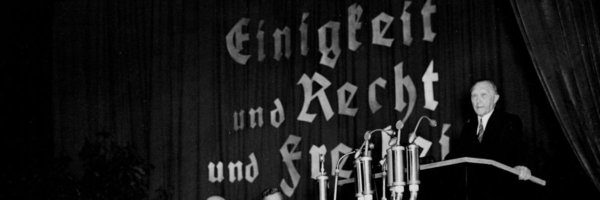 Adenauer vor einem Rednerpult und hinter ihm Schrift "Einigkeit und Recht und Freiheit"