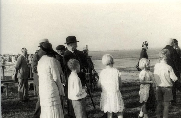 Schwarz-Weiss-Aufnahme von Konrad Adenauer neben Kindern und anderen Zuschauern auf einem Feld