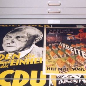Eine offene Schublade im Archiv, in der verschiedenen Wahlplakate aus der Adenauerzeit zu sehen sind. 