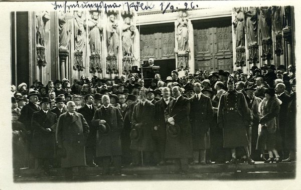 Schwarz-Weiss-Aufnahme von einer Gruppe Menschen und Konrad Adenauer am Rednerpult vor einem Kirchentor