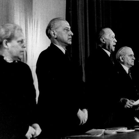 5 Personen und Konrad Adenauer, der etwas vorträgt, stehen