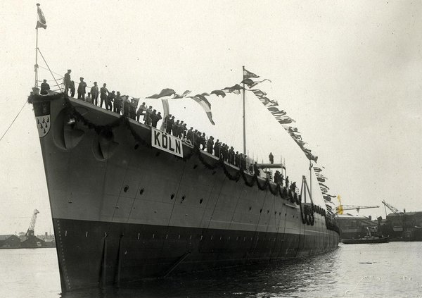 Schwarz-Weiss-Aufnahme von einem langen Schiff mit Personen an der Reling 