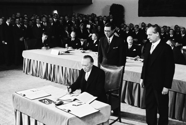 Schwarz-Weiss-Aufnahme von Konrad Adenauer beim Unterzeichnen des Deutschlandvertrages