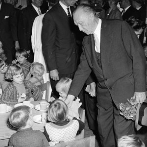 Adenauer steht neben eine Gruppe junger Kinder die an einem Tischchen Tee trinken.