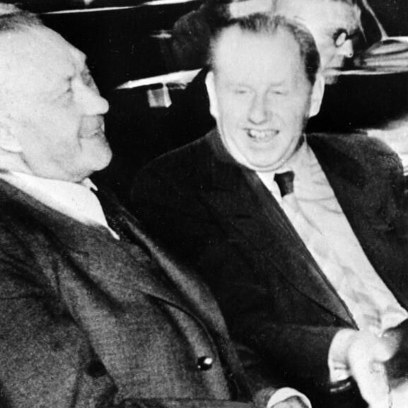 Friedrich Holzapfel und Konrad Adenauer sitzen nebeneinander und schmunzeln