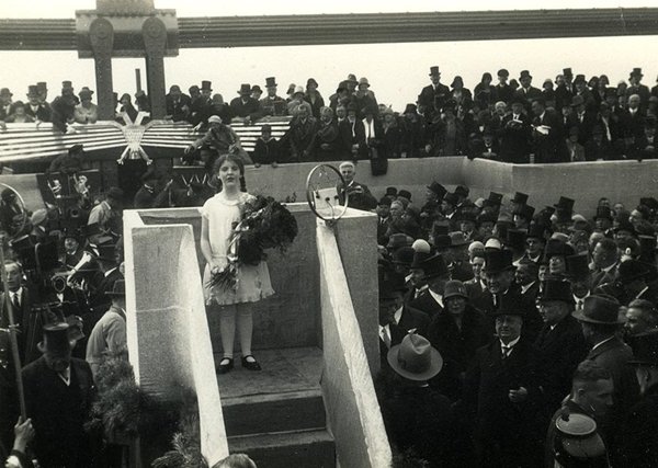 Schwarz-Weiss-Aufnahme von einem Mädchen in weißem Kleid und mit Rosenstrauß auf einer Empore vor dem Publikum