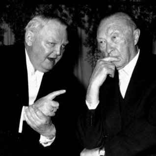 Ludwig Erhard und Konrad Adenauer sitzen zusammen an einem Tisch und unterhalten sich