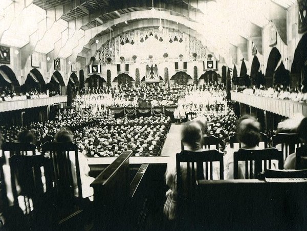 Schwarz-Weiss-Aufnahme von einer großen festlich geschmückten Halle voller Menschen