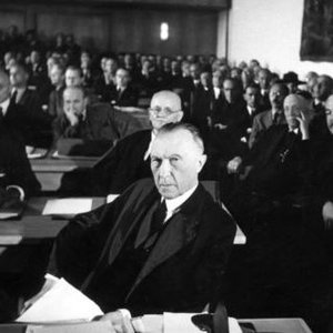 Konrad Adenauer sitzend in einem großen Saal mit vielen anderen Personen