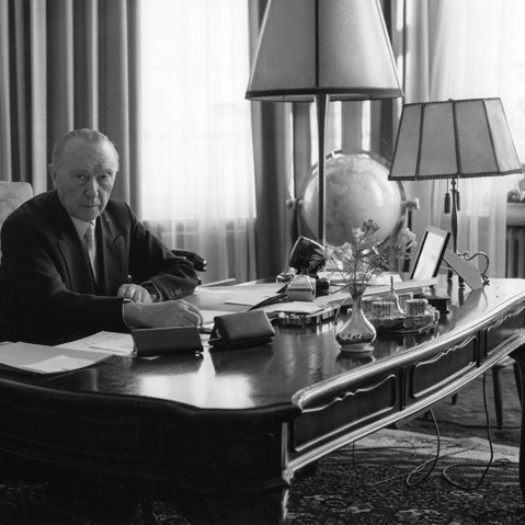 Schwarz-Weiss-Aufnahme von Konrad Adenauer am Schreitisch sitzend