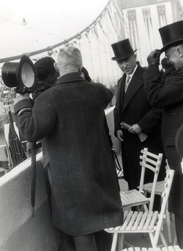 Schwarz-Weiss-Aufnahme von Konrad Adenauer mit anderen Personen vor der festlich geschmückten Mülheimer Brücke 