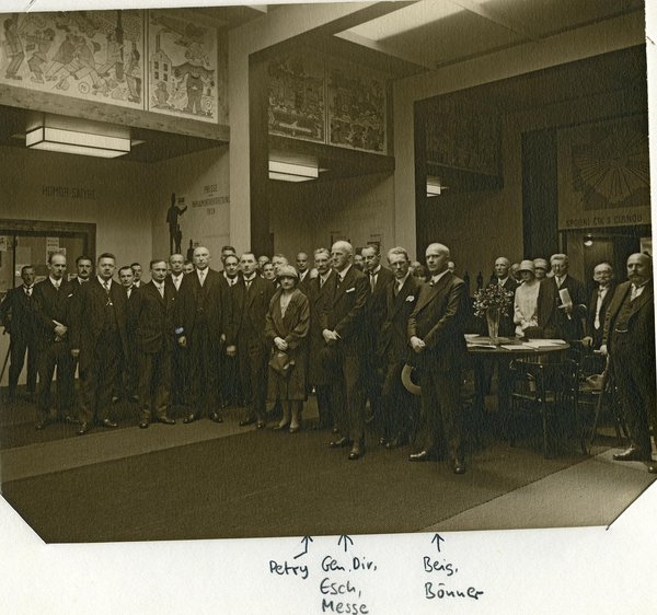 Schwarz-Weiss-Aufnahme von Konrad Adenauer mit einer Gruppe Menschen in einer Eingangshalle
