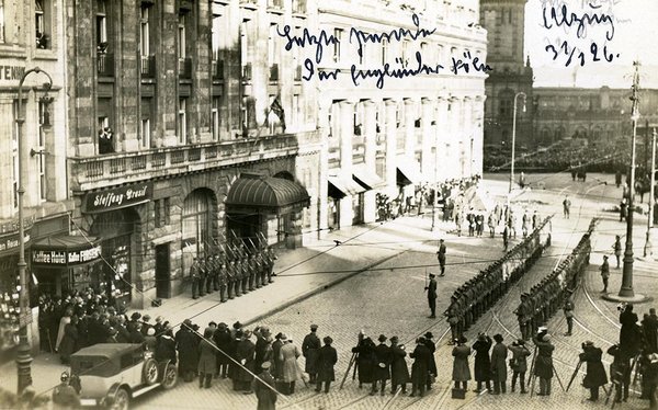 Schwarz-Weiss-Aufnahme von einem Straßenzug mit Militär und Zuschauern