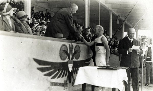 Schwarz-Weiss-Aufnahme von einem Sportler, der Konrad Adenauer an der Zuschauertribüne die Hand gibt