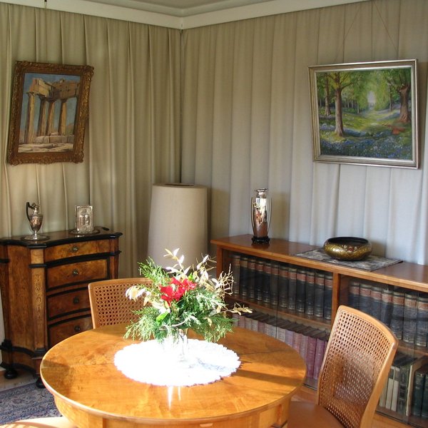 Ein gemütlich eingerichtetes kleines Zimmer mit Tisch, Stühlen und Kommoden.